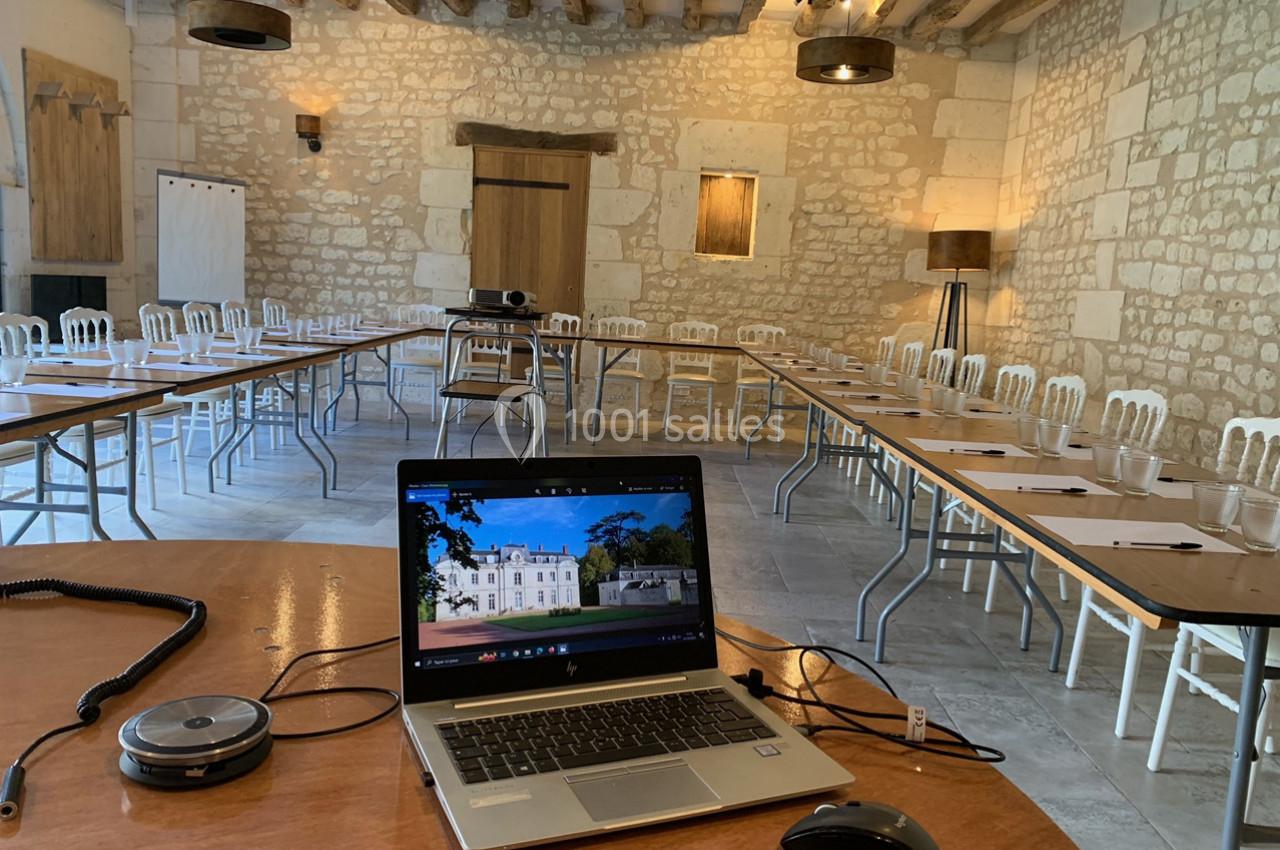 Salle de réunion en pierre avec tables disposées en U, équipée d'un ordinateur portable, d'un projecteur et de chaises.