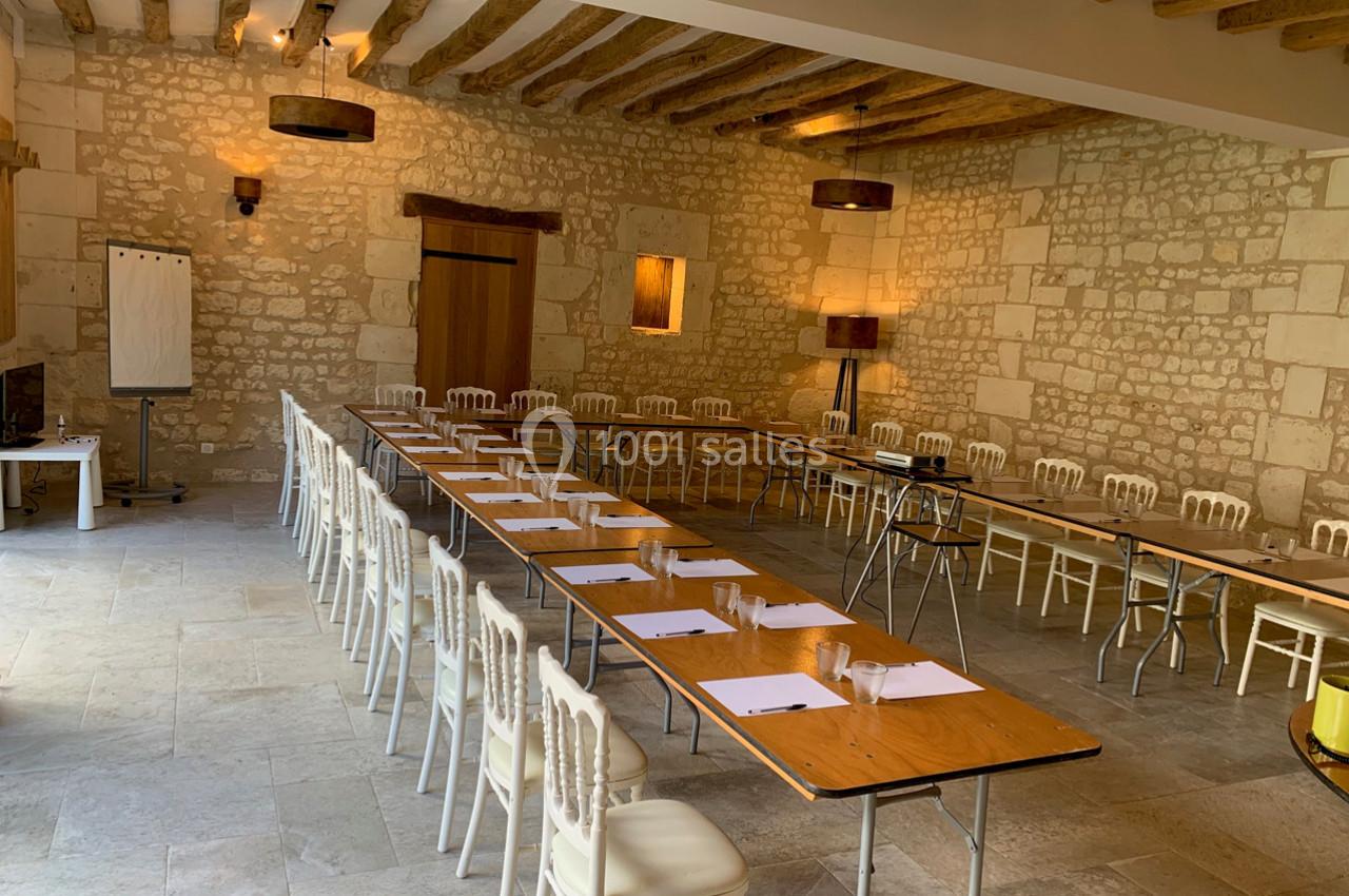 Salle de réunion lumineuse avec murs en pierre, tables disposées en U et chaises blanches alignées.