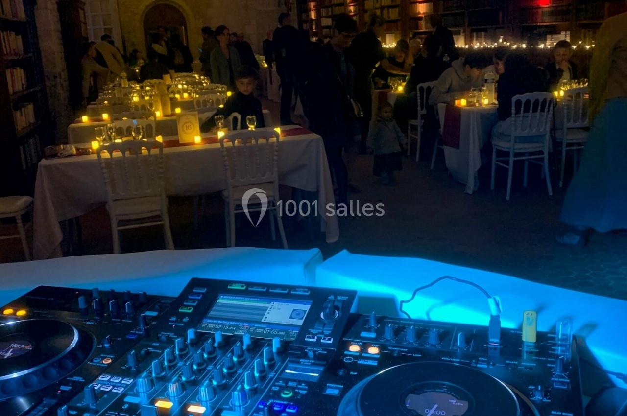 Console DJ éclairée au premier plan, avec une salle de réception décorée et des invités en arrière-plan.