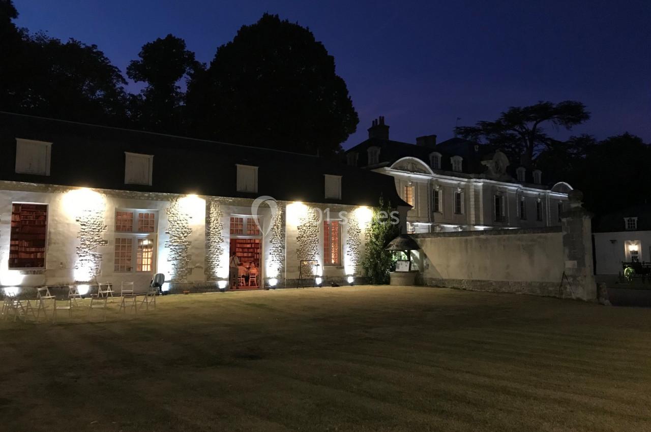 Bâtiment historique éclairé de nuit, avec une pelouse au premier plan et des arbres en arrière-plan.