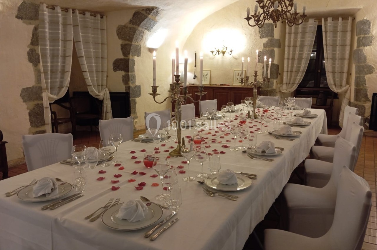 Table élégamment dressée dans une salle voûtée, ornée de chandeliers, pétales rouges et serviettes pliées.