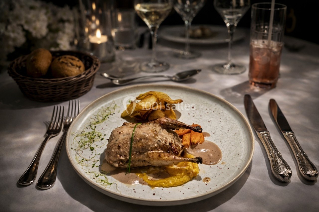 Assiette de caille rôtie avec purée, chips de légumes et sauce, servie sur une table élégamment dressée.
