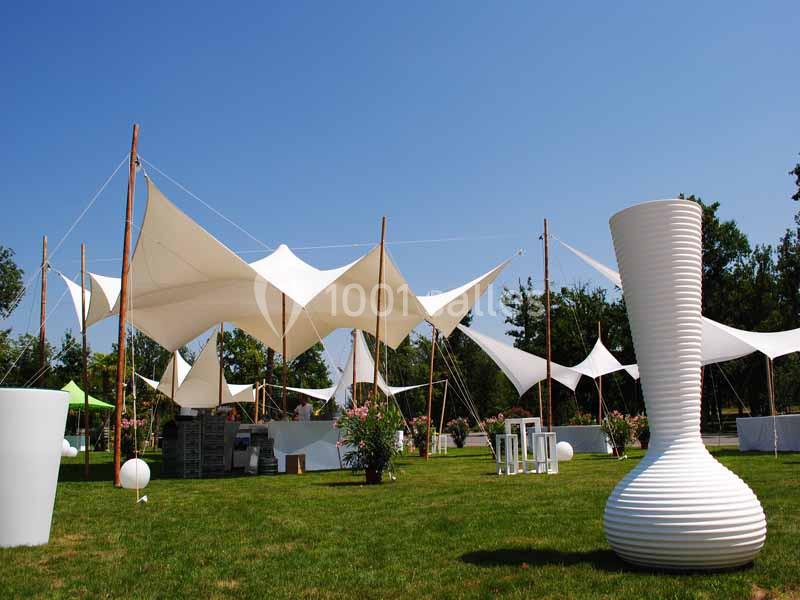 Structure en toile blanche tendue sur un espace extérieur avec pelouse, mobilier moderne et ciel dégagé.
