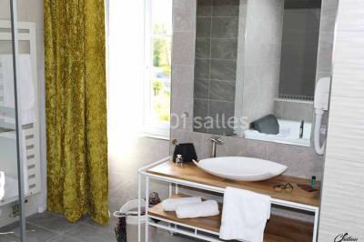 Salle de bain lumineuse avec lavabo sur meuble en bois, miroir mural, rideau jaune et fenêtre donnant sur l'extérieur.