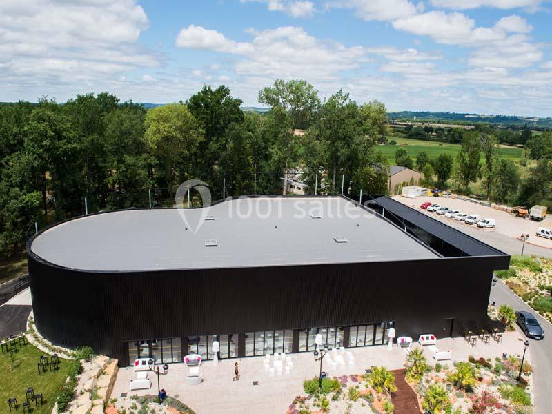 Vue aérienne d'un bâtiment moderne noir entouré de végétation, avec un parking et des aménagements paysagers.