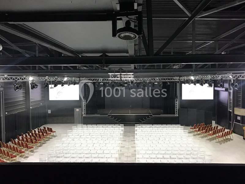 Salle de spectacle vide avec des rangées de chaises blanches et rouges face à une scène équipée de projecteurs.