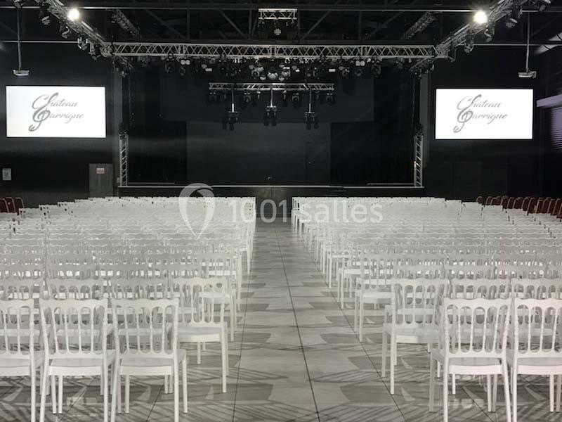 Salle de spectacle avec des rangées de chaises blanches alignées face à une scène équipée d'écrans et de projecteurs.