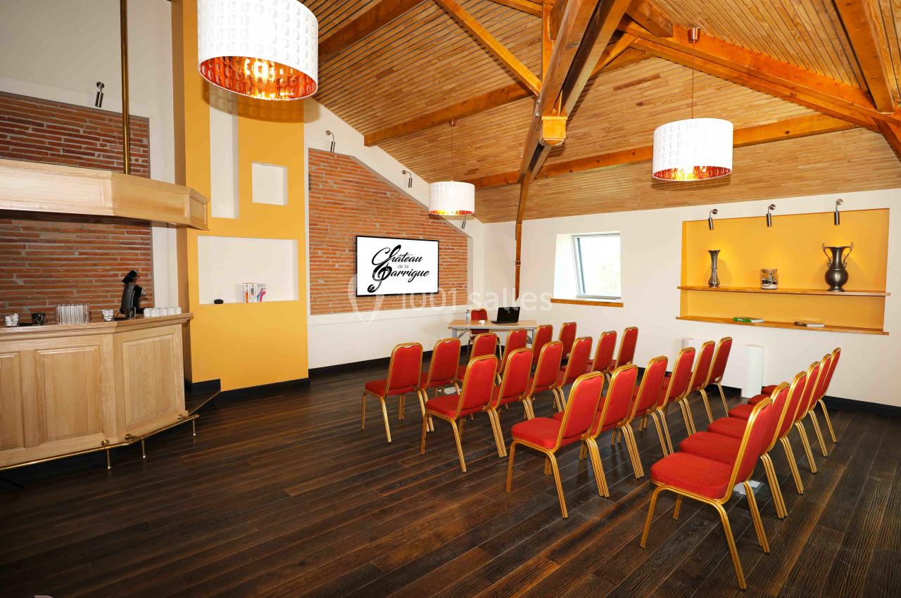 Salle de réunion avec chaises rouges alignées, écran de présentation, bar en bois et plafond en poutres apparentes.