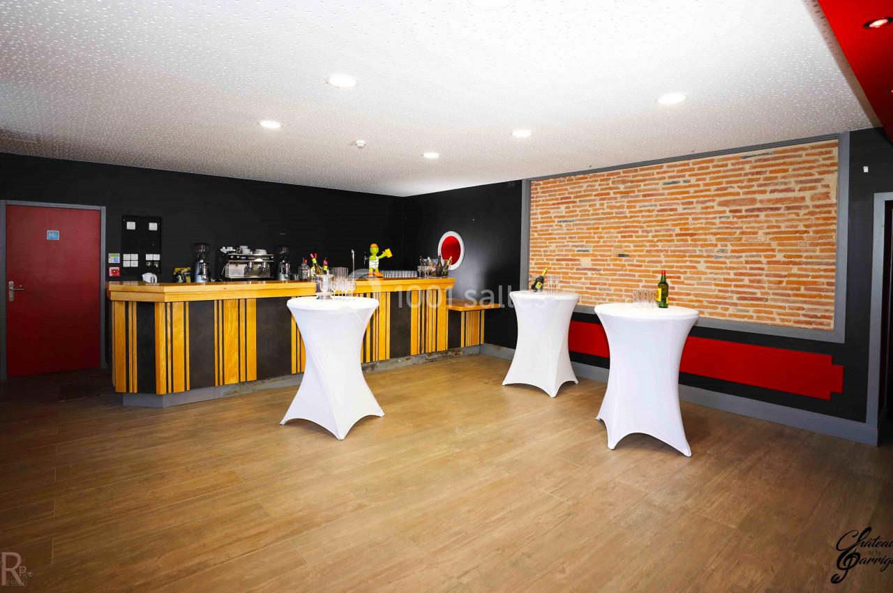 Salle avec un comptoir en bois, tables hautes drapées de blanc et mur en briques apparentes, éclairée par des spots.