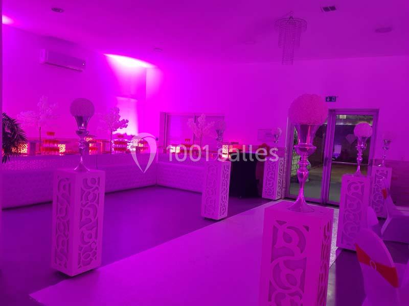 Salle de réception décorée de colonnes blanches et éclairée par une lumière rose.