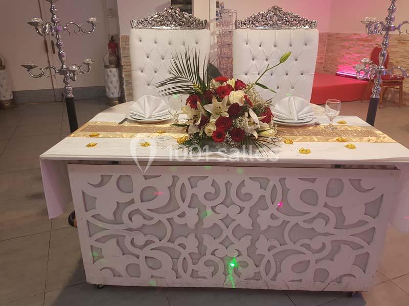 Table décorée pour un mariage avec un centre de table floral, deux chaises ornées et des chandeliers en arrière-plan.