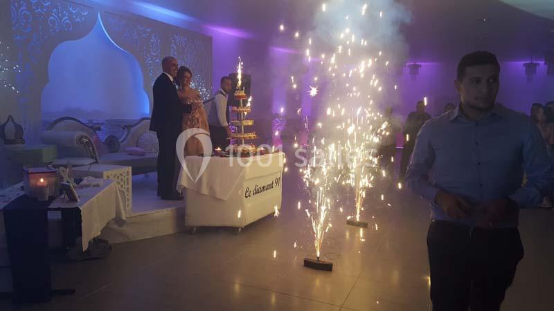 Un couple debout près d'une pièce montée entourée de fontaines lumineuses dans une salle décorée.