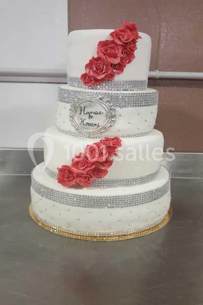 Gâteau de mariage à trois étages décoré de roses rouges, rubans argentés et inscription personnalisée.