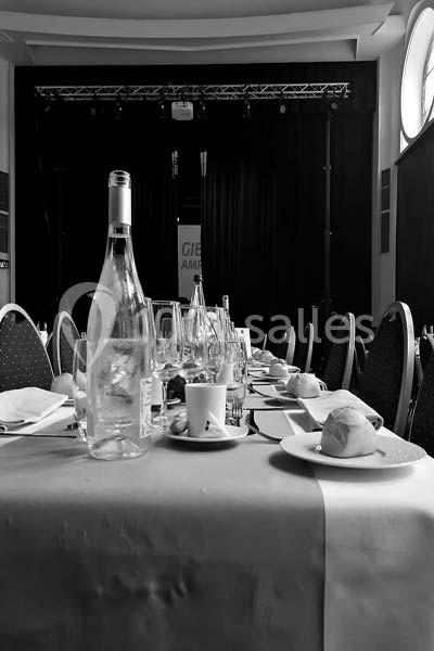 Table dressée avec des assiettes, verres et bouteilles dans une salle sombre avec une scène en arrière-plan.