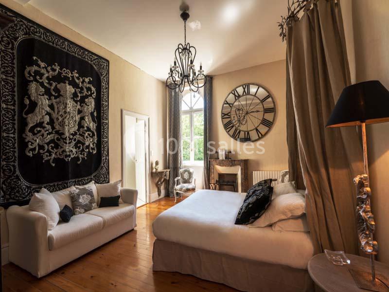 Chambre lumineuse avec lit double, canapé, grande horloge murale, tapis mural noir et lustre décoratif.