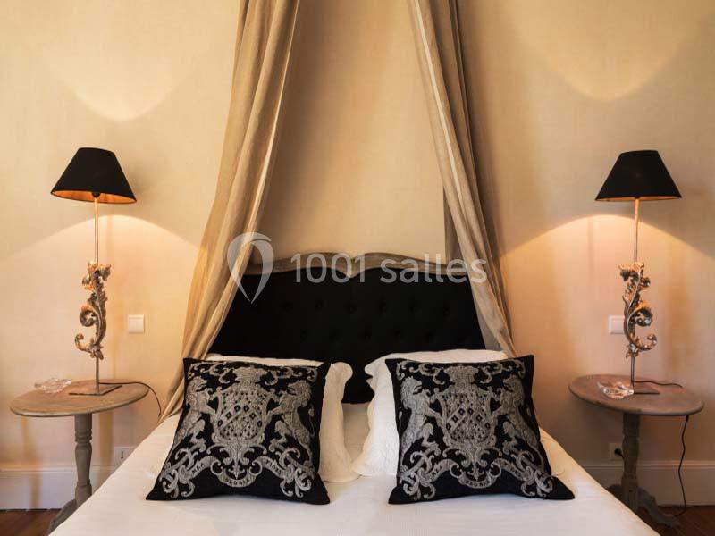 Lit double avec tête de lit capitonnée noire, deux coussins décoratifs et lampes de chevet sur des tables assorties.