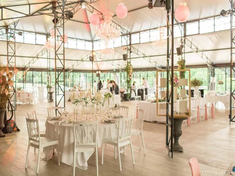 Salle de réception lumineuse avec tables décorées de nappes blanches, chandeliers et chaises blanches.