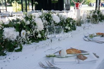 Table en bois dressée avec vaisselle, verres, fruits et fleurs, dans une salle lumineuse au décor chaleureux.