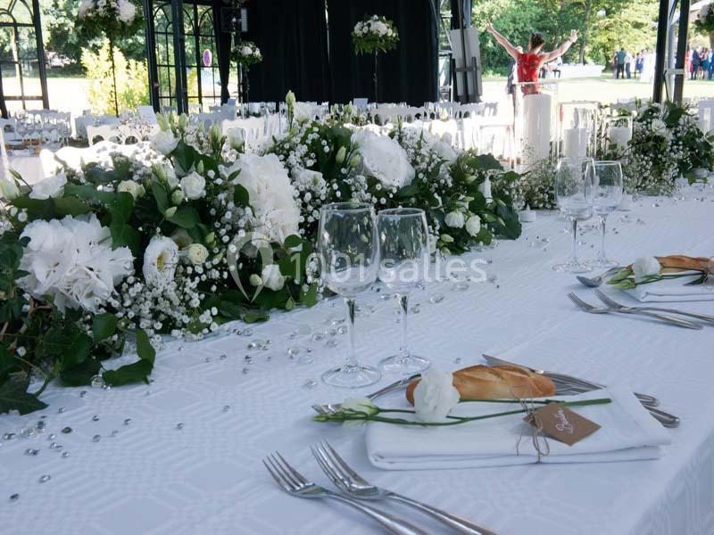Table décorée pour un mariage avec nappes blanches, compositions florales, verres, couverts et petits pains.