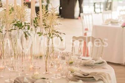 Table en bois dressée avec vaisselle, verres, fruits et fleurs, dans une salle lumineuse au décor chaleureux.
