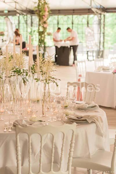Salle de réception lumineuse avec tables décorées de bougies et fleurs, et deux personnes en arrière-plan.
