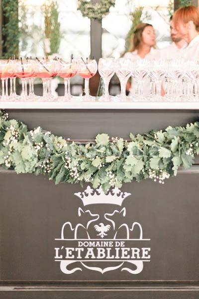 Comptoir décoré de feuillage avec des verres à cocktail alignés, logo ’Domaine de l'Établière’ visible en bas.