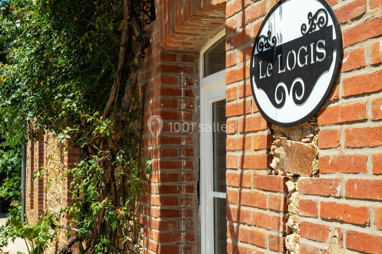 Façade en briques avec une porte blanche, une enseigne ’Le Logis’ et un auvent en fer forgé.