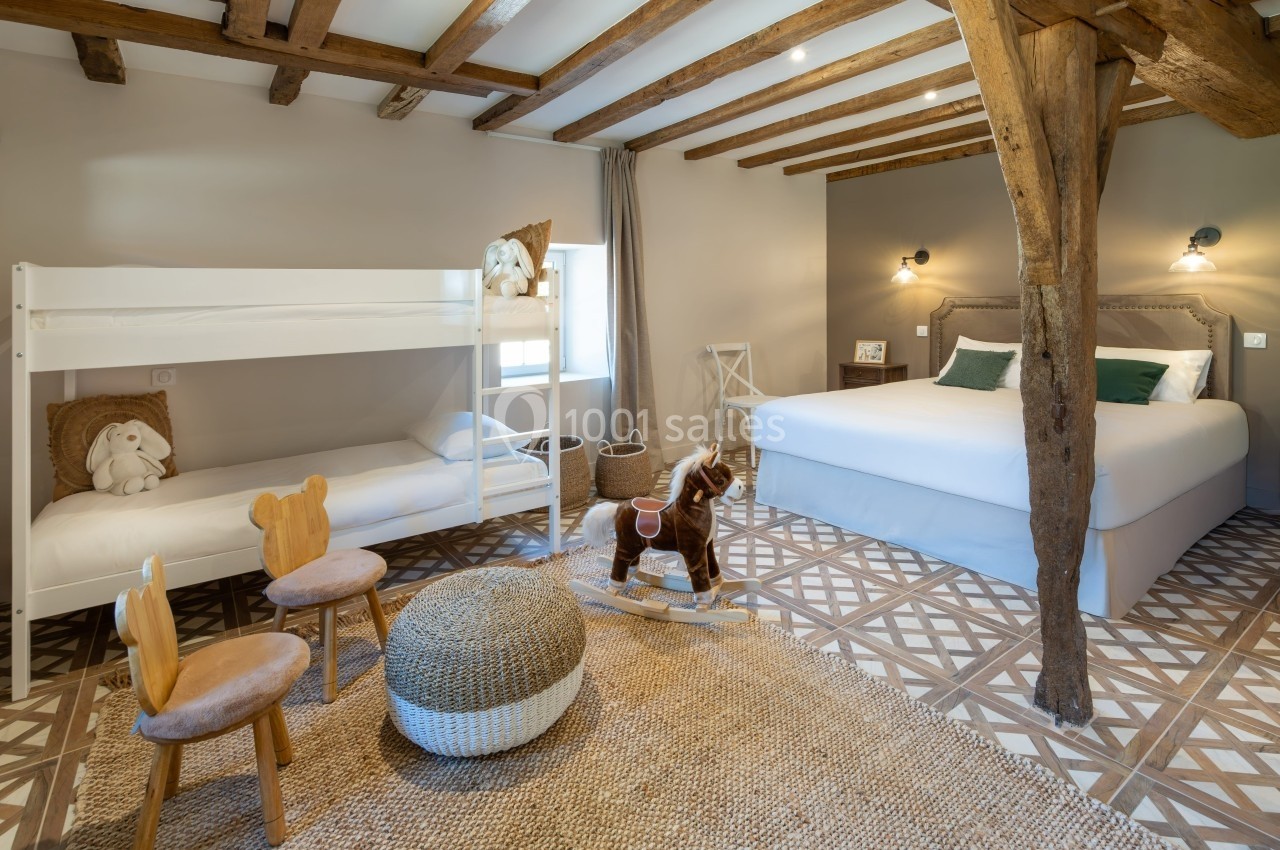 Chambre lumineuse avec lits superposés, lit double, poutres apparentes, jouets en bois et décoration chaleureuse.