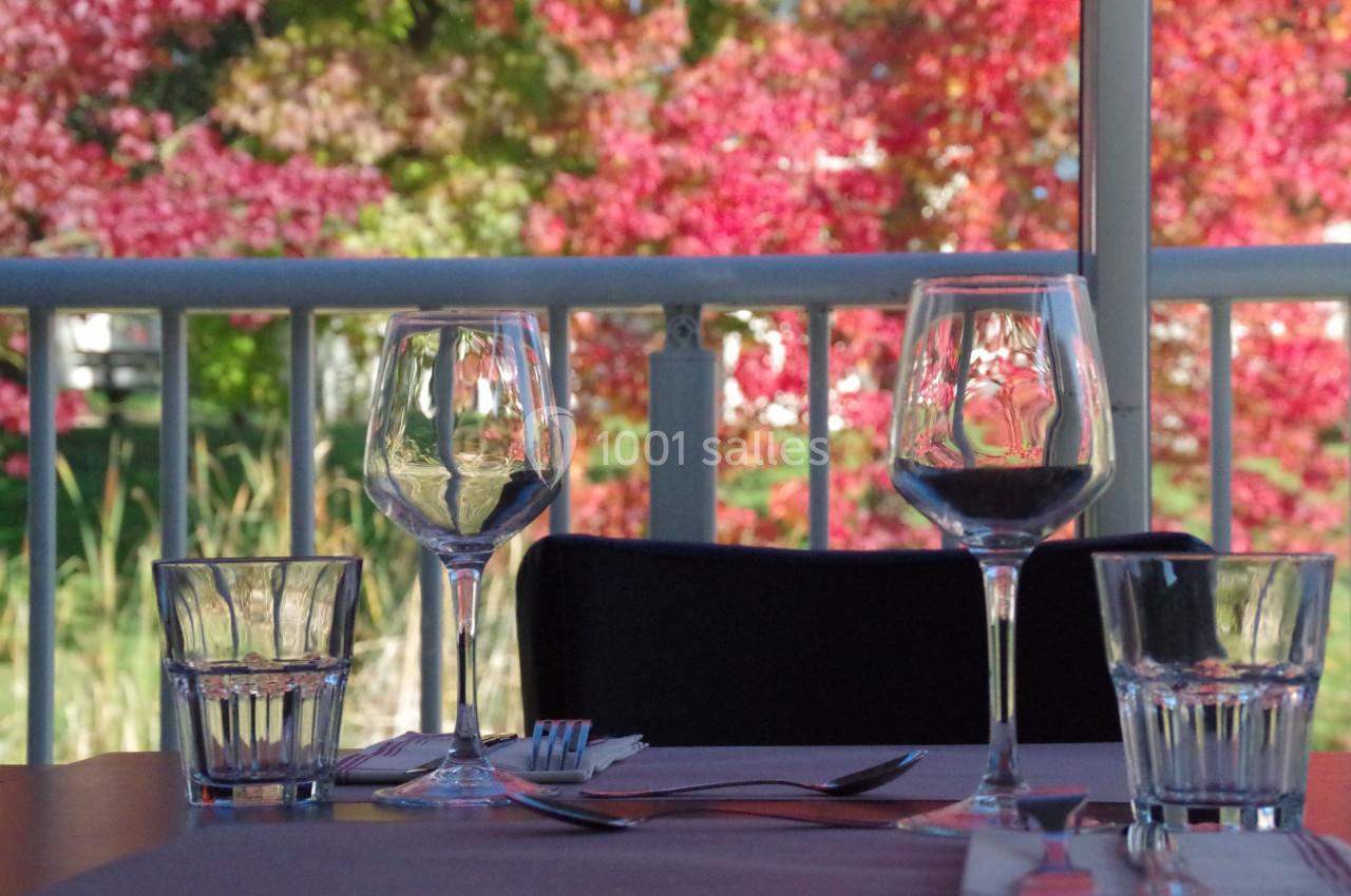 Verres à vin et à eau disposés sur une table, avec des arbres aux feuilles rouges visibles en arrière-plan.