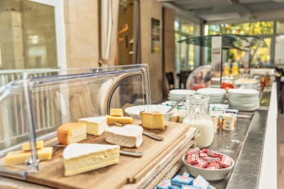 Plateau de fromage avec raisins et pain en arrière-plan, un verre de vin rosé au premier plan.