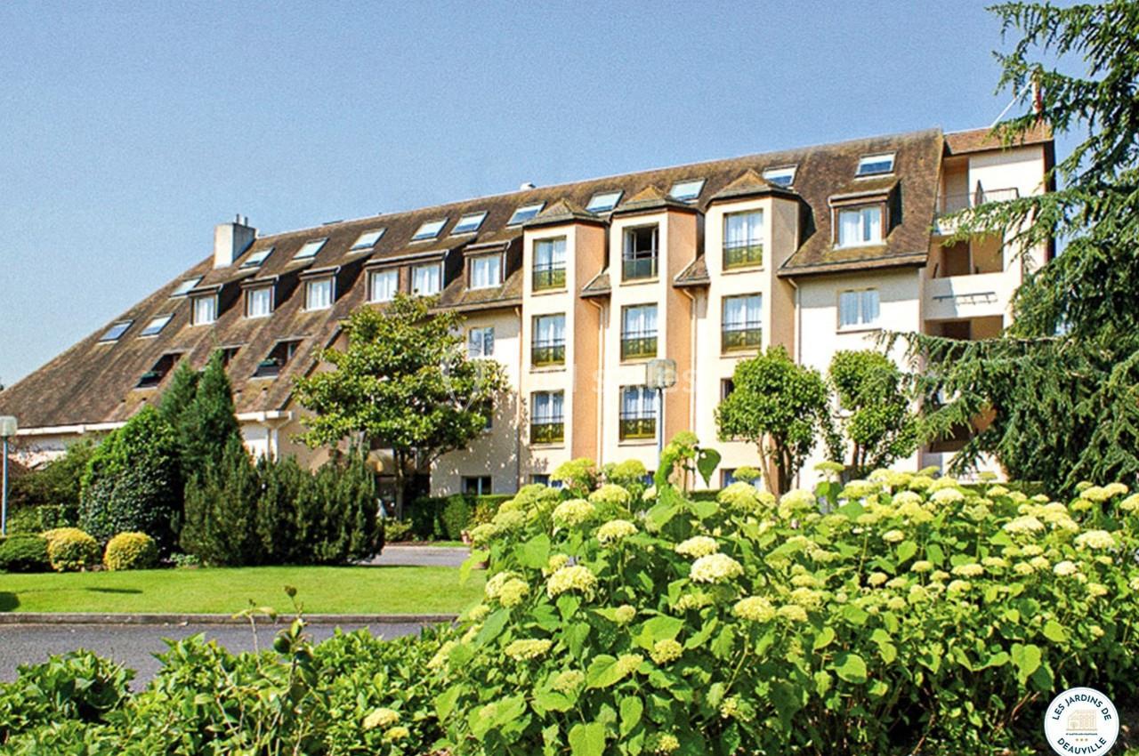 Bâtiment résidentiel entouré de jardins verdoyants avec des arbustes et des fleurs au premier plan.