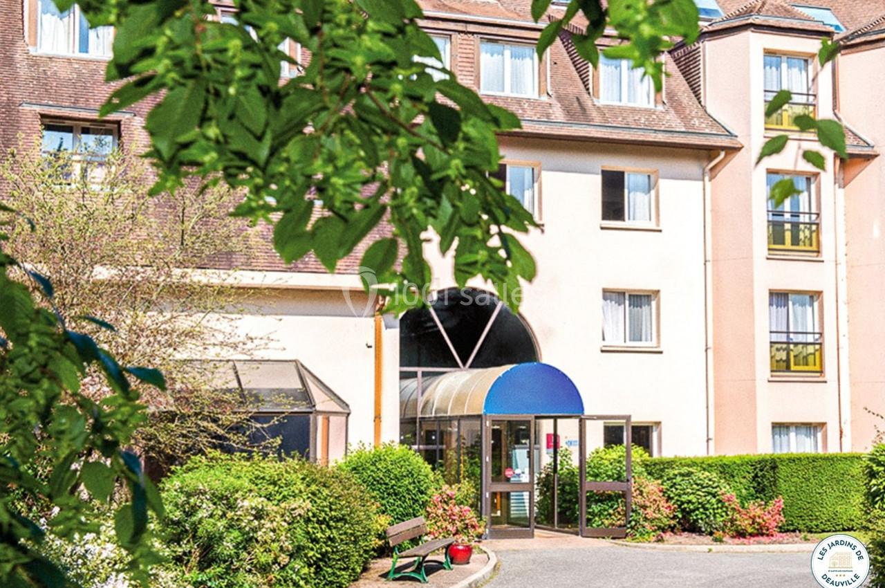 Façade d'un bâtiment résidentiel avec entrée vitrée, entourée de végétation et d'un banc au premier plan.