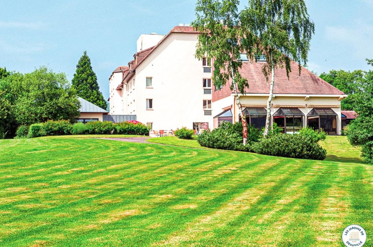 Bâtiment clair entouré d'un grand jardin verdoyant avec pelouse bien entretenue et arbres en arrière-plan.