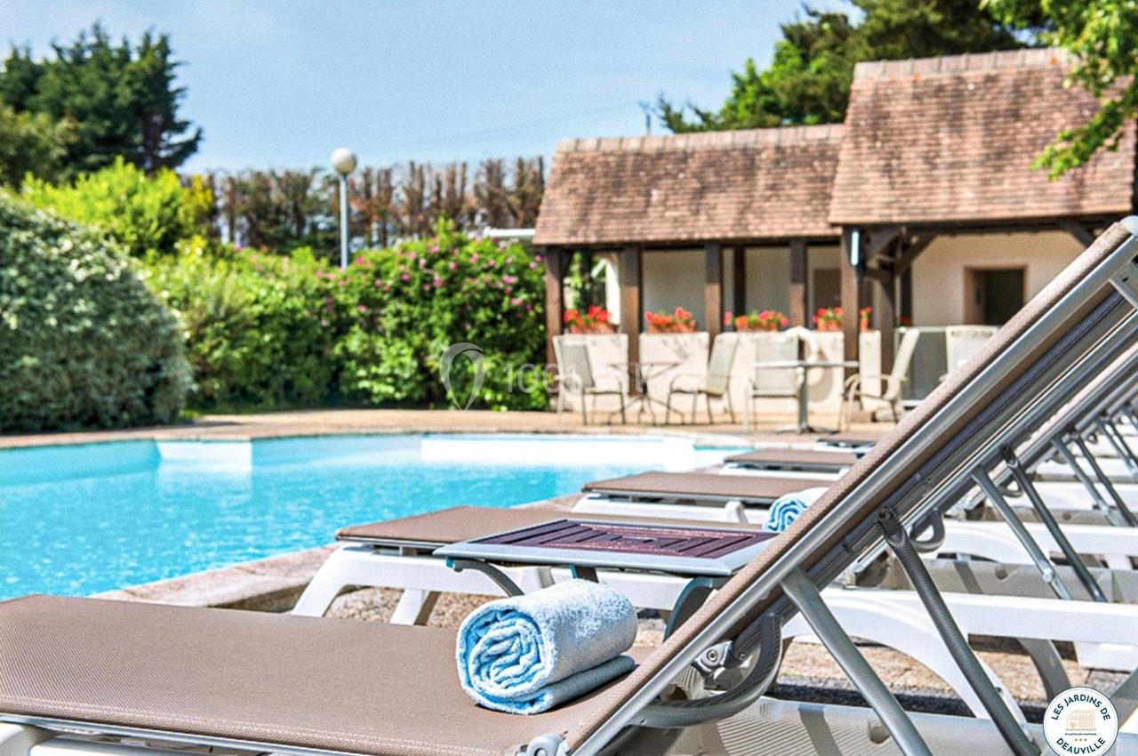 Transats alignés près d'une piscine extérieure, entourée de verdure et d'un bâtiment au toit en tuiles.