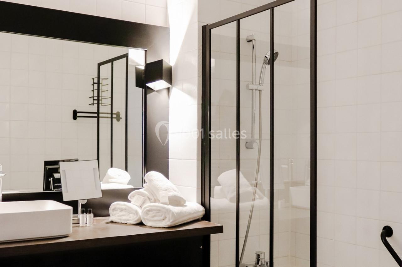 Salle de bain moderne avec douche vitrée, lavabo rectangulaire, miroir éclairé et serviettes pliées sur le comptoir.