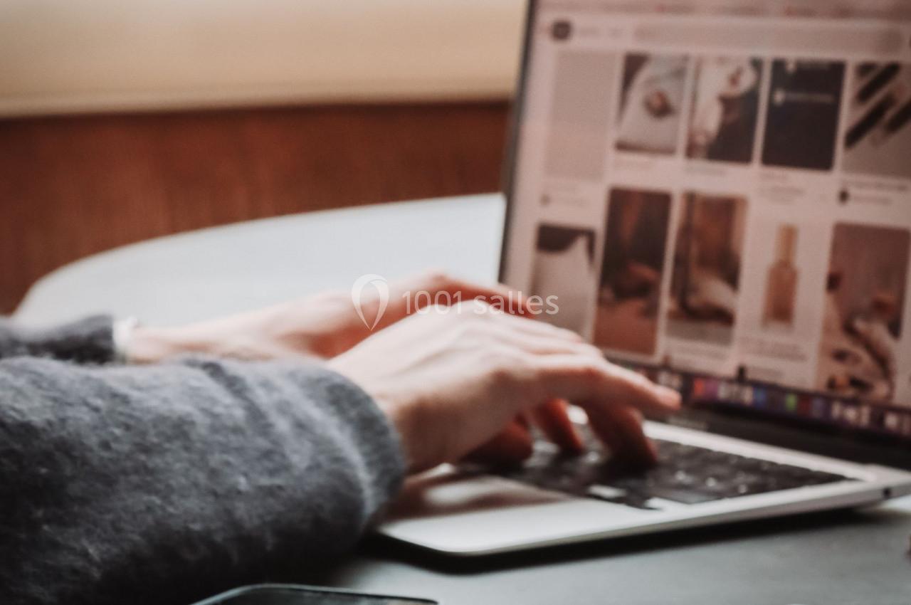 Personne utilisant un ordinateur portable, avec des crayons et un smartphone posés sur une table.