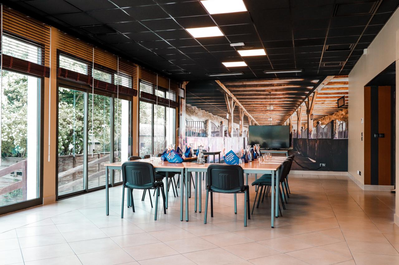 Salle de réunion lumineuse avec de grandes baies vitrées, des chaises et une table rectangulaire.