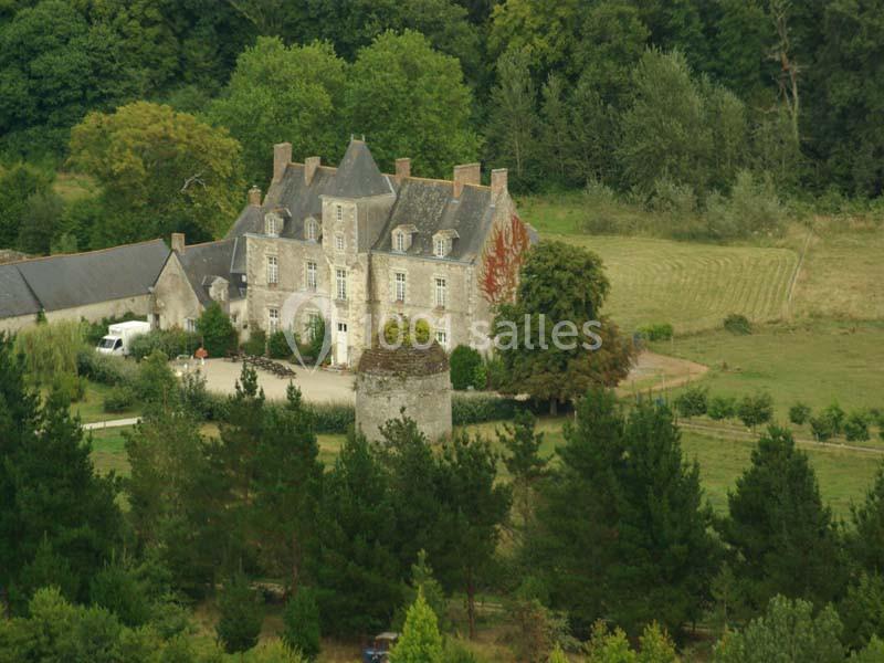 Manoir ancien entouré de verdure, avec une tour en pierre au premier plan et des arbres en arrière-plan.