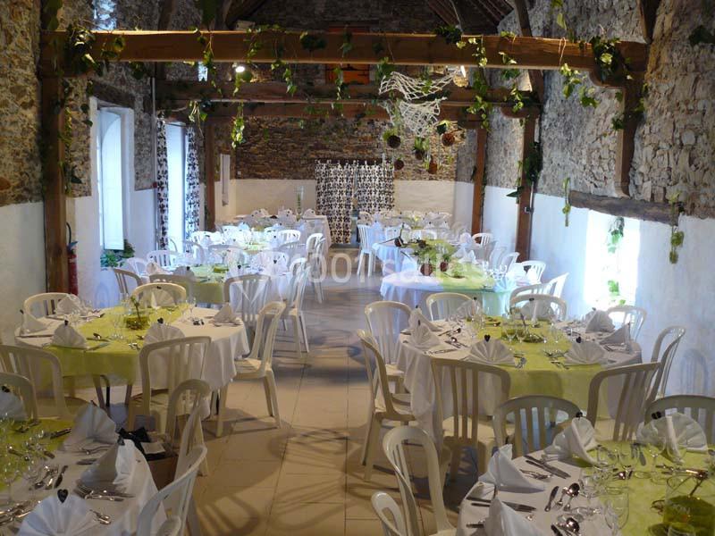 Salle de réception rustique décorée avec des tables rondes, nappes vertes et blanches, et chaises en plastique.