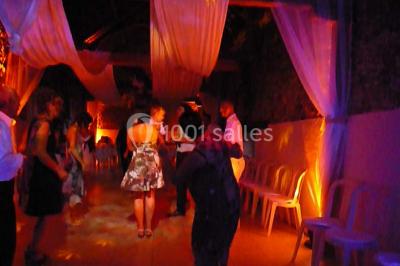 Deux personnes en costume historique s'affrontent à l'épée dans une cour devant un mur en pierre avec des arches.