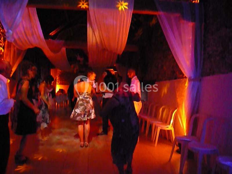 Des personnes dansent sous des lumières colorées dans une salle décorée de rideaux blancs et de chaises alignées.