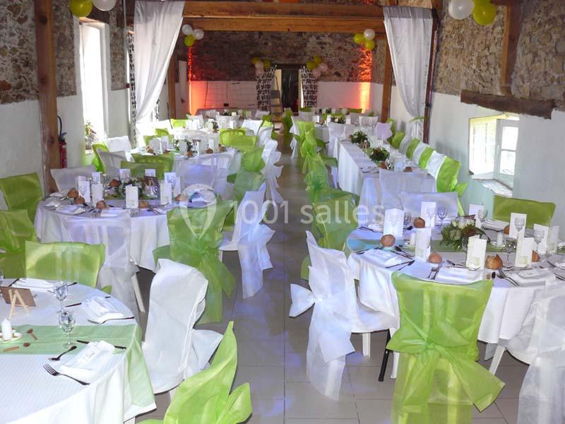 Salle de réception décorée pour un événement, avec des tables dressées et des chaises ornées de nœuds verts et blancs.