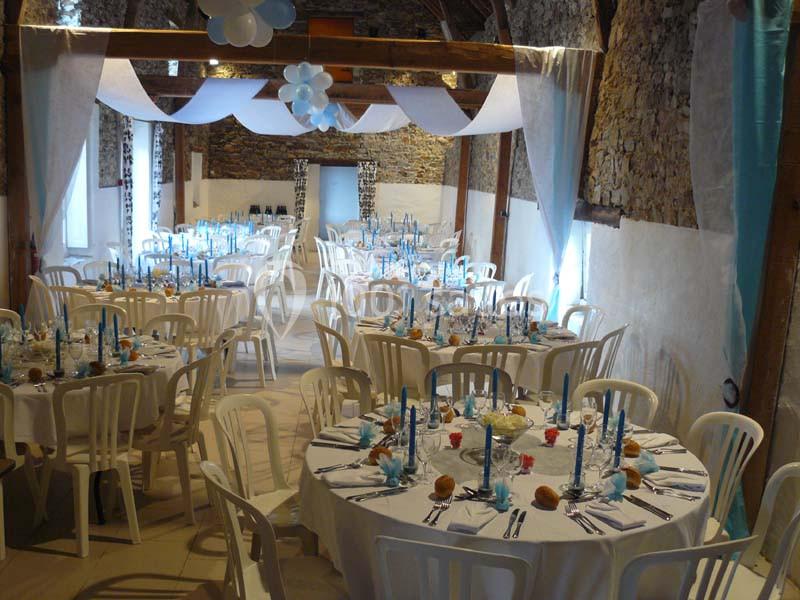 Salle de réception décorée avec des tables rondes, nappes blanches, bougies bleues et éléments de décoration suspendus.