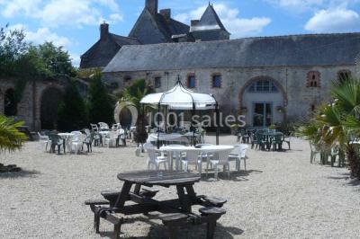 Deux personnes en costume historique s'affrontent à l'épée dans une cour devant un mur en pierre avec des arches.