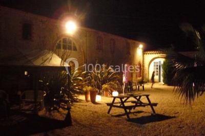 Deux personnes en costume historique s'affrontent à l'épée dans une cour devant un mur en pierre avec des arches.