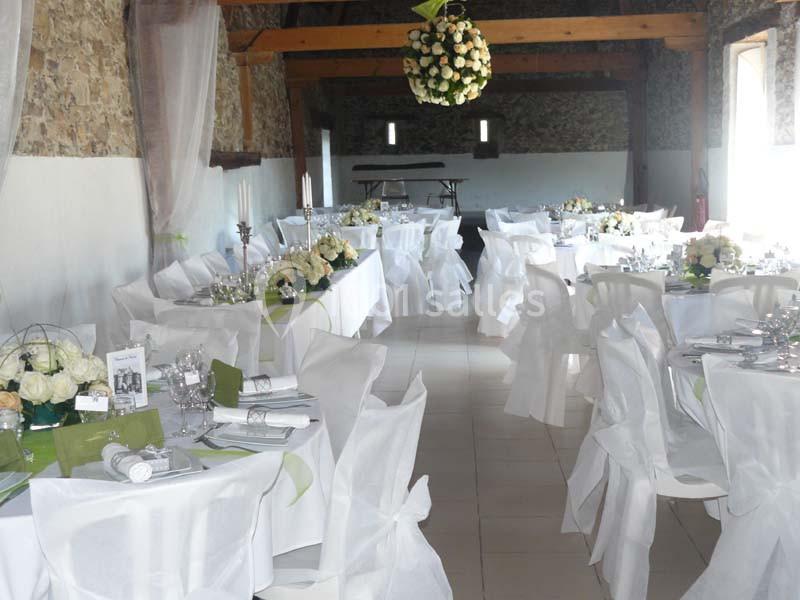 Salle de réception décorée avec des tables dressées, nappes blanches, chaises couvertes et centre de table floral.