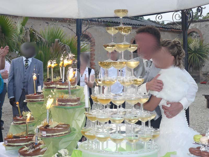 Un couple de mariés devant une pyramide de coupes de champagne et des gâteaux décorés de bougies et de feux d'artifice.