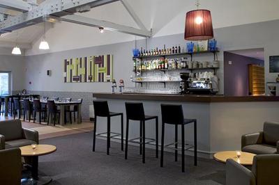 Salle de restaurant moderne avec tables alignées, chaises noires et décoration murale colorée sur le thème de la…