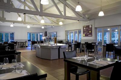 Salle de restaurant moderne avec tables alignées, chaises noires et décoration murale colorée sur le thème de la…
