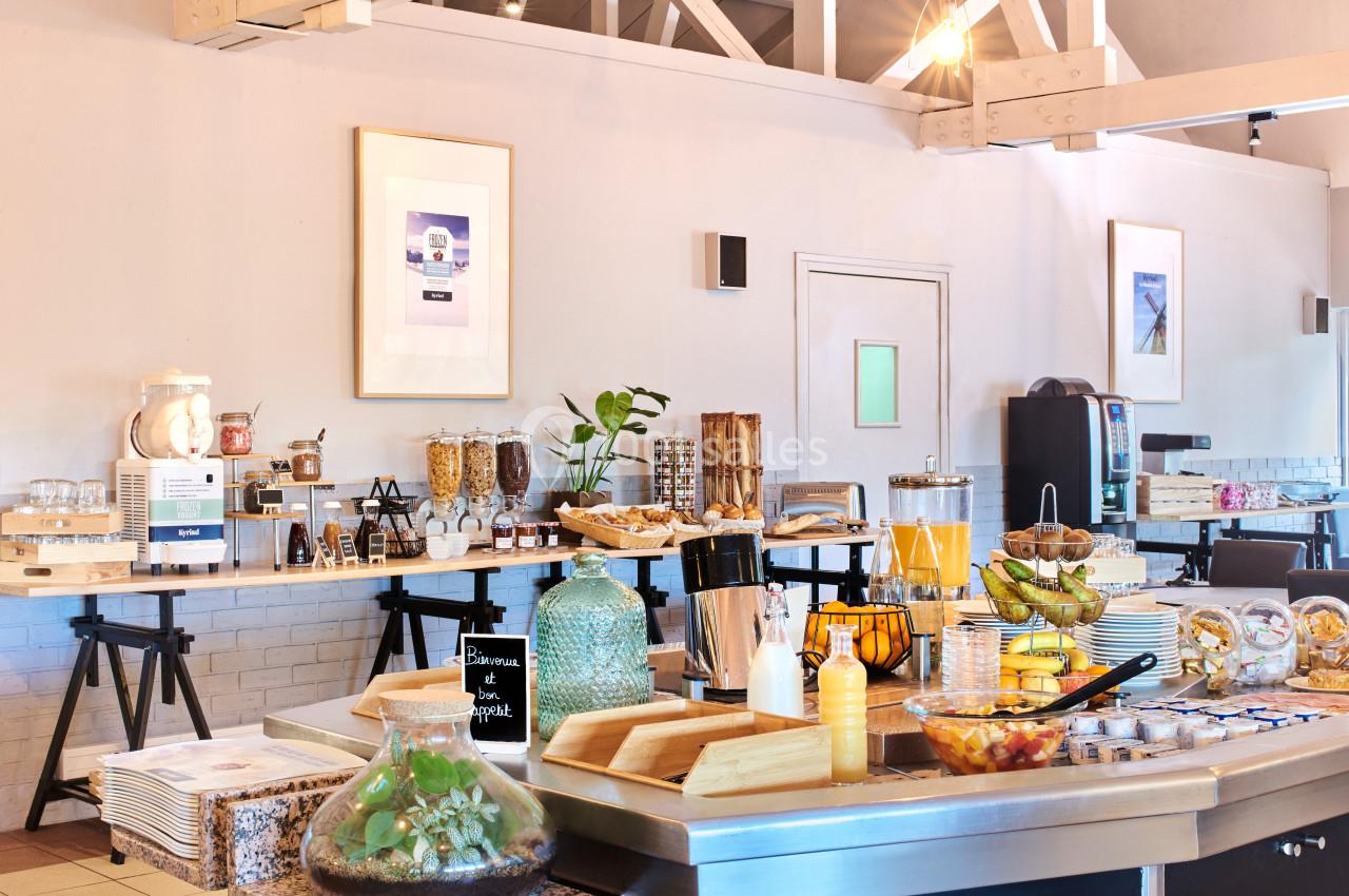 Buffet de petit-déjeuner avec boissons, fruits, céréales, viennoiseries et divers aliments disposés sur des tables.